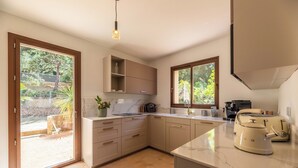 Una cucina moderna con una grande isola, mobili a incasso e vista sul giardino attraverso un'ampia porta scorrevole in vetro.