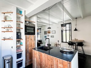 A modern kitchen with wooden cabinetry, a central island, and a dining area with a table and chairs. - Holiday Home Henriette: authentic house in the centre of Bergen (Bergen (NH))