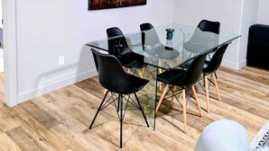 A modern dining area with a glass table and black chairs, a wooden floor, and a large abstract painting on the wall.