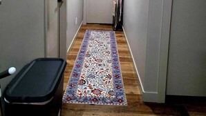 A narrow hallway with a patterned rug, wooden flooring, and a white door at the end.