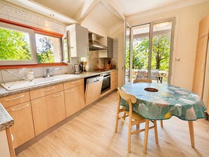 A kitchen with wooden cabinets, a sink, and a dining area with a table and chairs. - Air-conditioned house with enclosed garden, 3 bedrooms, quiet location near Cahors (Pradines)