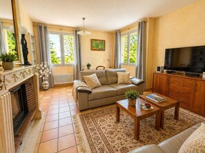 A living room with a sofa, TV, fireplace, and large windows. - Air-conditioned house with enclosed garden, 3 bedrooms, quiet location near Cahors (Pradines)