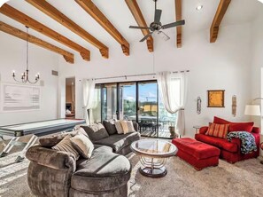 A spacious living room with a sofa, ottoman, and a round coffee table. There is a ceiling fan, a chandelier, and a large window with curtains. - Desert Escape in the Foothills!
Family friendly with pool and views (Tucson)