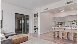 A modern living room with a sofa, ottoman, and a kitchen area with a bar and stools. - Desert Escape in the Foothills!
Family friendly with pool and views (Tucson)