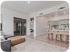 A modern living room with a sofa, ottoman, and a kitchen area with a bar and stools. - Desert Escape in the Foothills!
Family friendly with pool and views (Tucson)