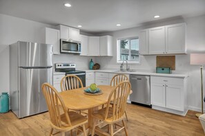 A modern kitchen with white cabinets, stainless steel appliances, a wooden dining table, and a teal vase.