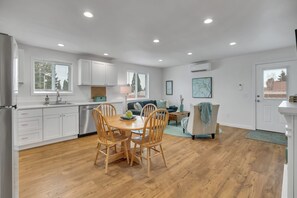 A modern kitchen with white cabinets, a dining table with chairs, and a wooden floor.