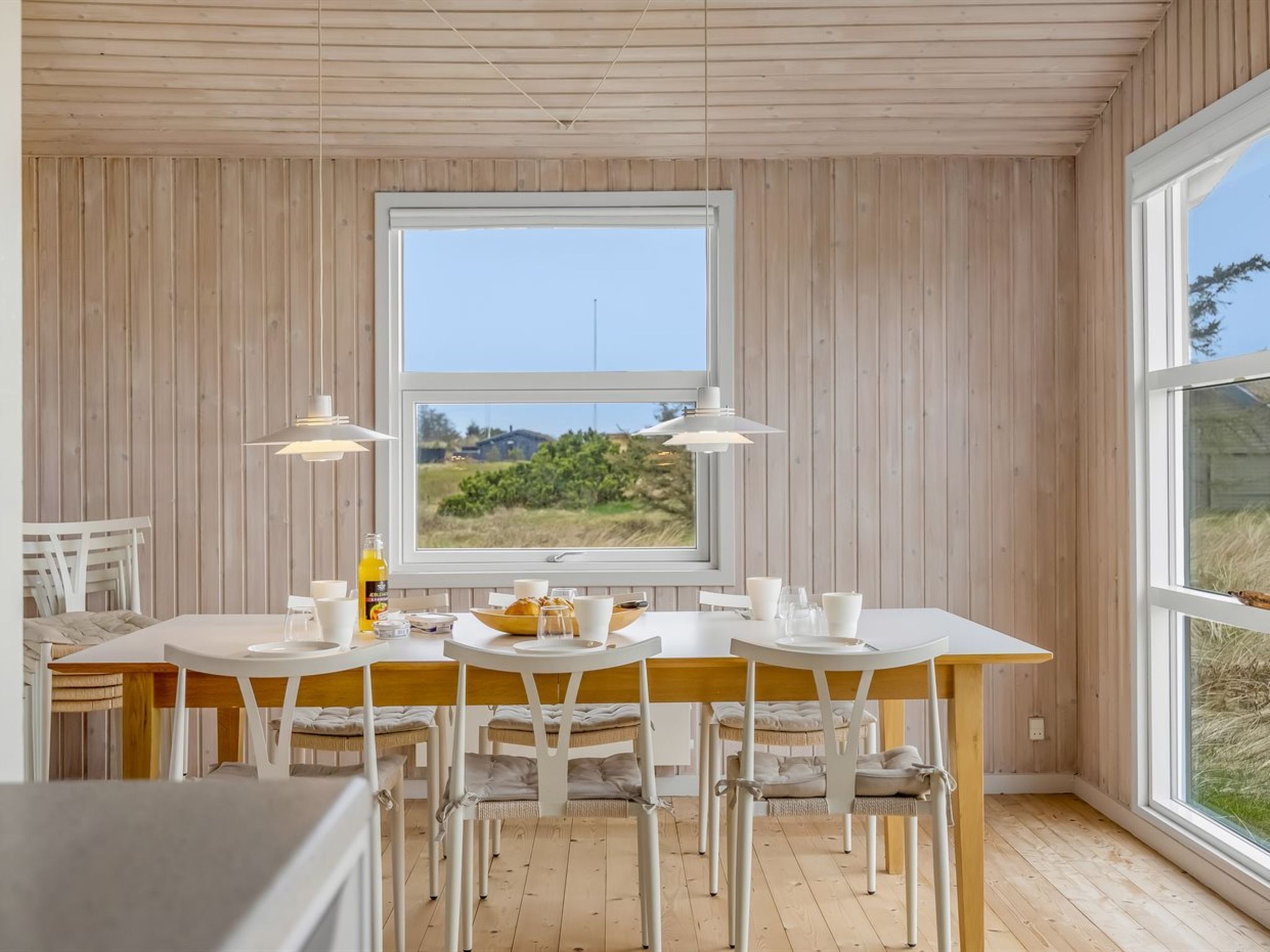 Ein Essbereich mit großem Fenster, Holzwänden und Blick ins Grüne.