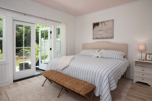 Ein Schlafzimmer mit Bett, Bank, Nachttisch und Blick durch eine Glastür.