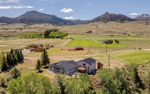 Uma casa moderna com um deck espaçoso, cercada por campos abertos e montanhas.