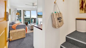 Un interior moderno con sofá, mobiliario de mimbre, zona de comedor y vistas amplias por grandes ventanales.