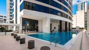 A modern hotel with a rooftop pool, lounge chairs, and a view of surrounding buildings.