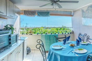 Une cuisine équipée d’un four Brandt, une table à manger recouverte d’une nappe bleue et un balcon agrémenté de plantes et offrant une vue.