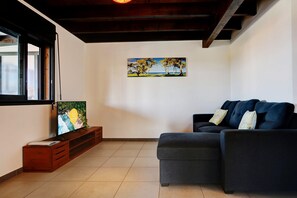 Ein Wohnzimmer mit einem dunklen Sofa, einer Holz-Unterhaltungsanlage und einem Gemälde mit einer Strandansicht.