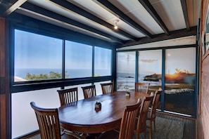 A dining area with a large wooden table and chairs, large windows with ocean views, and a ceiling with exposed beams. - Kaz Bois Blanc - AC - Vue mer - Avirons (Les Avirons)