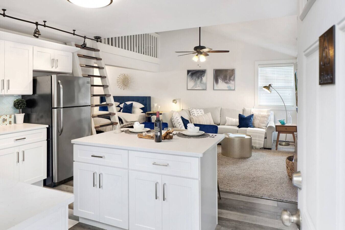 A modern kitchen with white cabinetry, a stainless steel refrigerator, and a dining area with a white table and blue accents.
