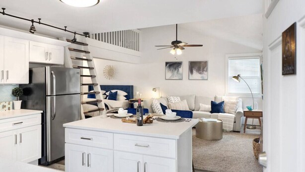 Una cucina moderna con mobili bianchi, un frigorifero in acciaio inossidabile e un'area pranzo con tavolo bianco e dettagli blu.