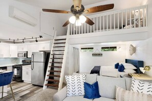 Ein modernes Interieur mit einer Küche, einem Essbereich und einem Schlafzimmer auf dem Dachboden mit einer Treppe.
