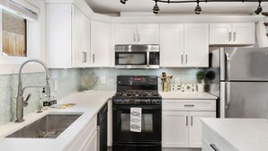 Una cucina moderna con mobili bianchi, elettrodomestici in acciaio inossidabile, piano cottura a gas e forno a microonde integrato.