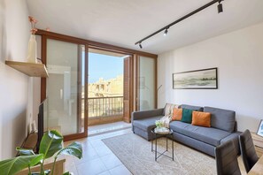 Una sala de estar moderna con un sofá gris, una mesa de centro y un ventanal con vistas a edificios.