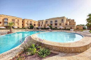 A hotel with a large pool, outdoor seating, and a Mediterranean architectural style. - Fort Chambray Gozo 2BDR Apartment (Ghajnsielem)