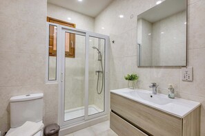 A modern bathroom with a glass-enclosed shower, a white sink with a wooden vanity, and a mirror above the sink. - Fort Chambray Gozo 2BDR Apartment (Ghajnsielem)