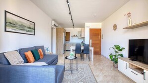 Ein modernes Wohnzimmer mit grauem Sofa, einem Flachbildfernseher und einem Essbereich mit Tisch und Stühlen.