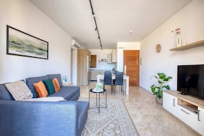A modern living room with a grey sofa, a flat-screen TV, and a dining area with a table and chairs. - Fort Chambray Gozo 2BDR Apartment (Ghajnsielem)
