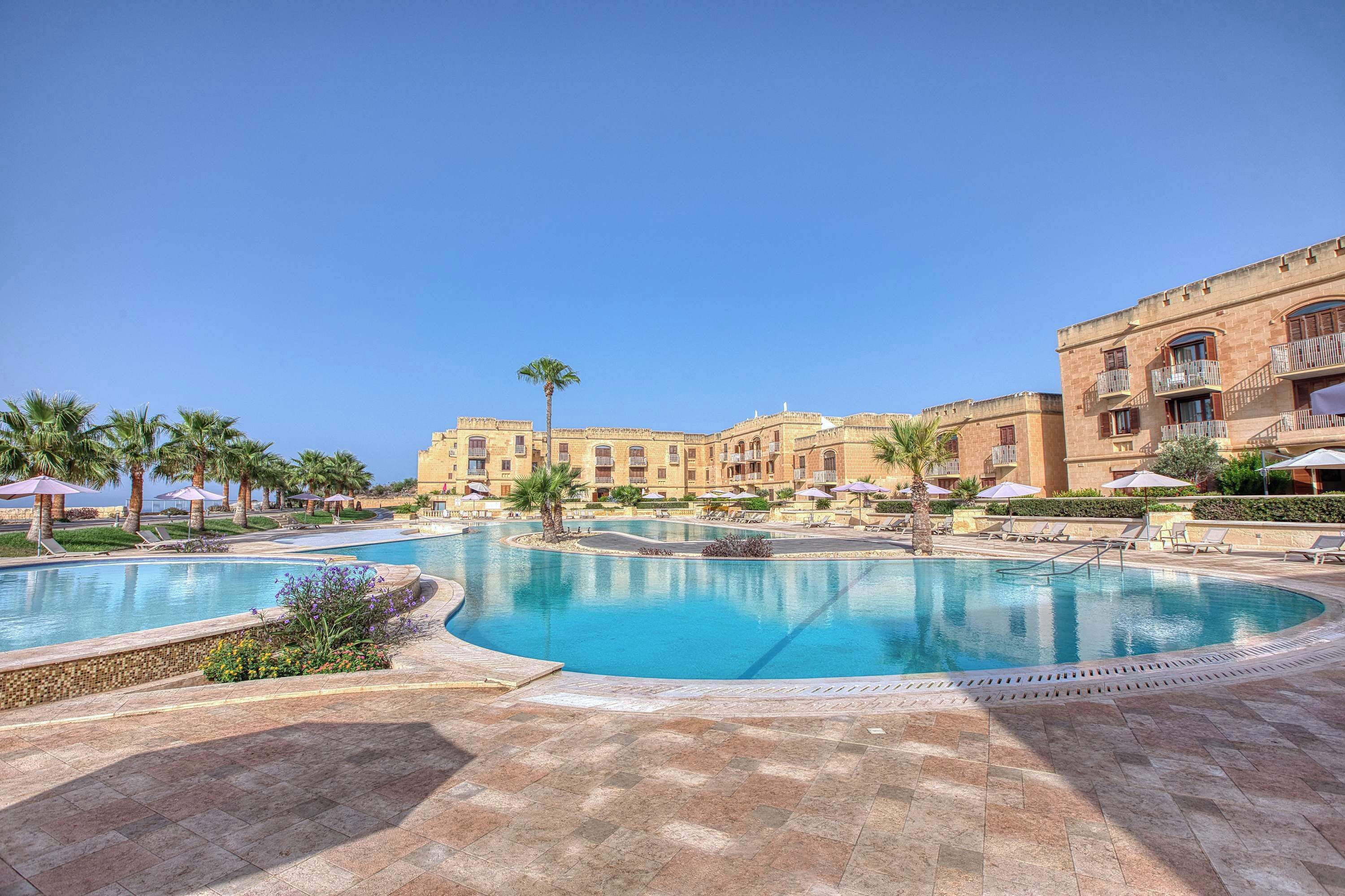 A resort with a large swimming pool, palm trees, and a multi-story building with balconies.