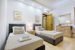 A hotel room with two beds, a wooden wardrobe, a bedside table with a lamp, and a large mirror. - Fort Chambray Gozo 2BDR Apartment (Ghajnsielem)
