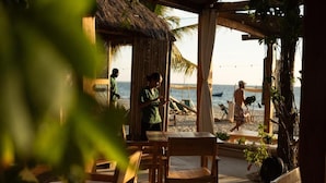 A beachside seating area with wooden tables and chairs, a thatched-roof structure, and a view of the ocean. - Dos Aguas Lodge (Rincón del Mar)