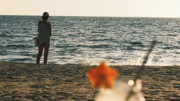 Escena de playa con una persona de pie en el agua y una bebida sobre una mesa al frente.
