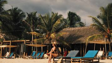 A beach with lounge chairs and a thatched-roof hut.