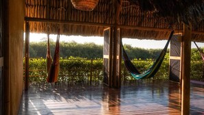 Une terrasse en bois avec un toit de chaume, un hamac et une vue sur la verdure.