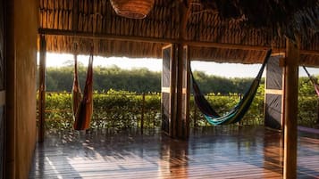 Une terrasse en bois avec un toit de chaume, un hamac et une vue sur la verdure.