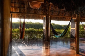 Una terraza de madera con techo de paja, una hamaca y vistas al verdor.