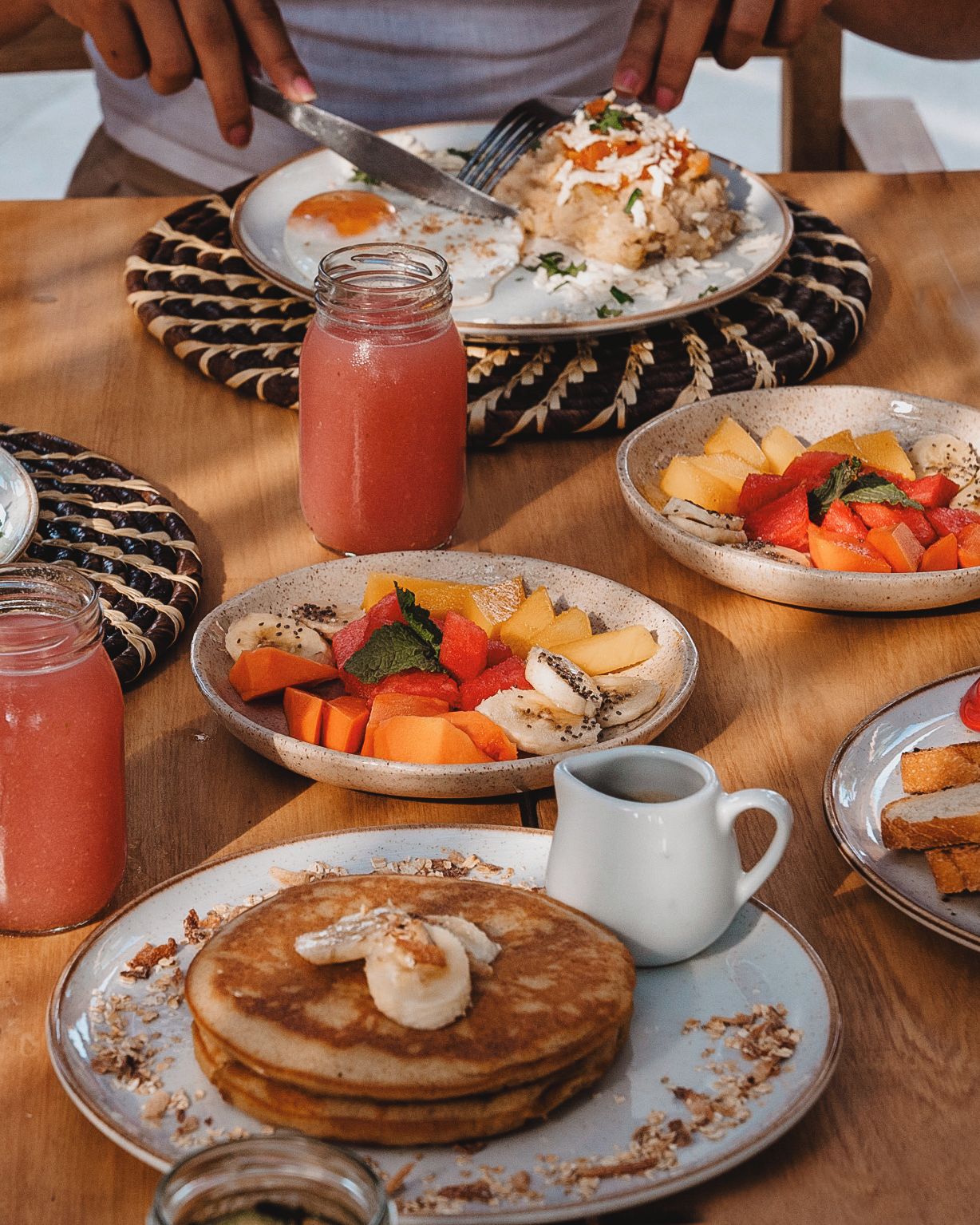 Disposição para o pequeno-almoço com panquecas, fruta e um smoothie sobre uma mesa de madeira.