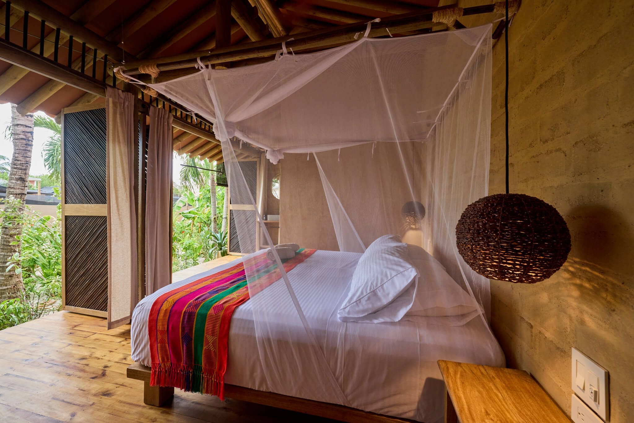 Una cama con dosel, una mesita de noche y vistas al verdor exterior.