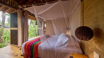Una cama con dosel, una mesita de noche y vistas al verdor exterior.