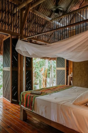 A room with a bed, a window with a view of greenery, and a wooden ceiling structure. - Dos Aguas Lodge (Rincón del Mar)