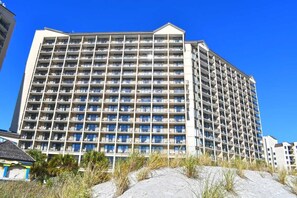 A multi-story hotel with a grid of balconies, located near a sandy area with sparse vegetation. - Amazing 1Bedroom Unit with Amazing Oceanfront View (North Myrtle Beach)