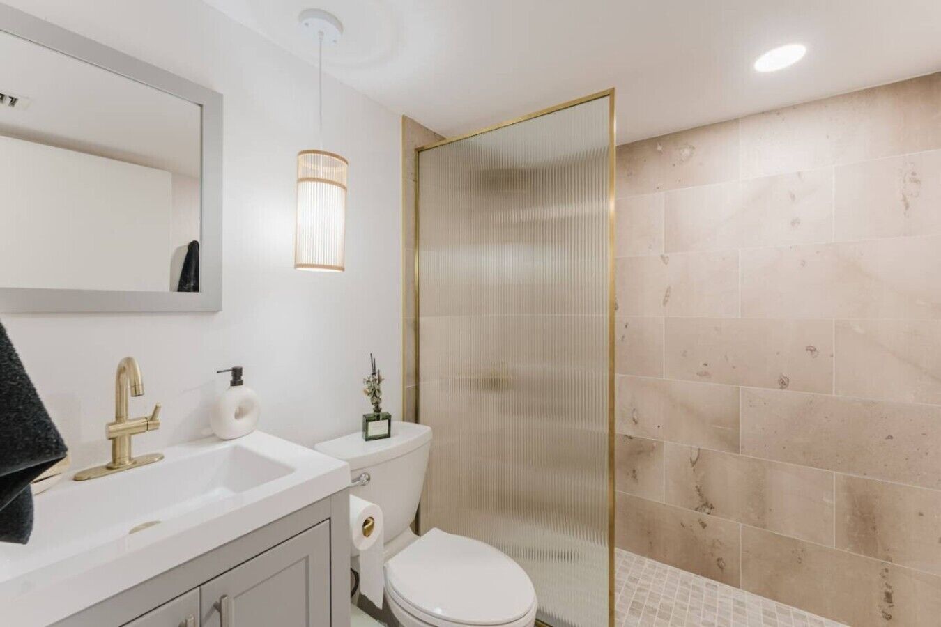 Une salle de bain avec un lavabo blanc, un robinet doré, des toilettes et une douche dotée d’un cadre doré.