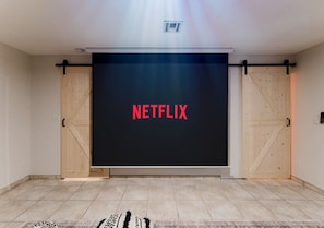 Habitación con una pantalla grande que muestra 'NETFLIX', puertas de madera y piso de baldosas.