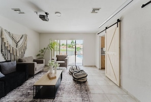 Una sala de estar con sofá, mesa de centro y otomanas, una puerta corrediza y vistas al exterior.