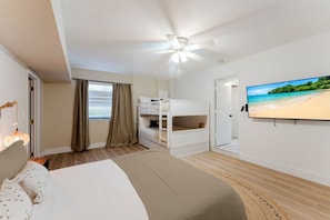 Un dormitorio con cama, literas, ventilador de techo, televisor y vista al mar.