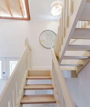 Una escalera con escalones de madera y barandas blancas, un espejo circular en la pared y una puerta al final.