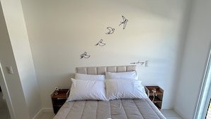 A bedroom with a large bed, two bedside tables, a wall with a bird decal, and a window. - House just 5 minutes from the beach. (Florianópolis)