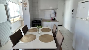 A modern kitchen with white cabinets, a dining table with placemats, and a refrigerator. - House just 5 minutes from the beach. (Florianópolis)
