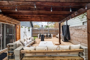An outdoor patio with a wooden deck, a seating area with cushions, a table, and string lights. - Cozy Walk to AT&T Stadium! Game Day Retreat!Family Friendl (Arlington)