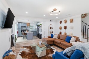 A modern living room with a brown sofa, a glass coffee table, and a kitchen in the background. - Cozy Walk to AT&T Stadium! Game Day Retreat!Family Friendl (Arlington)